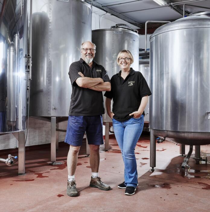 The owners of a brewery standing by large silver vats.