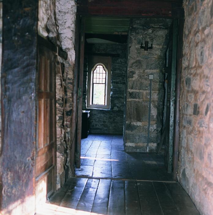 A stone brick corridor with and arched window at the end inside Gwydir Castle .