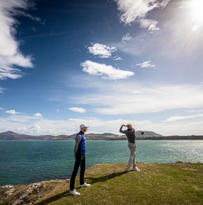 Golfers taking a swing on a headland by the sea.