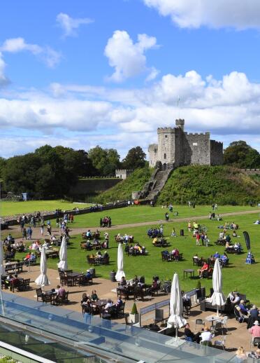 A castle and its keep behind lawns filled with people sitting on tables.