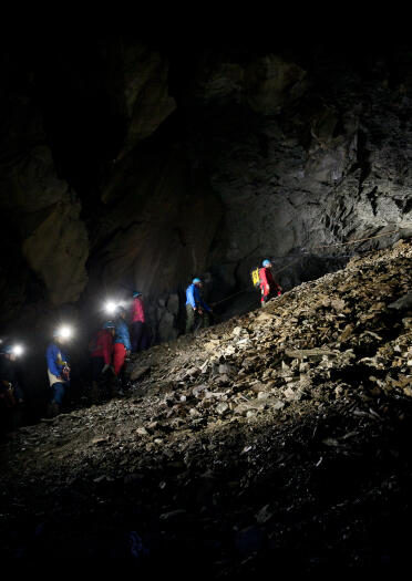 Explorers tied together and climbing up a slate heap in a mine.