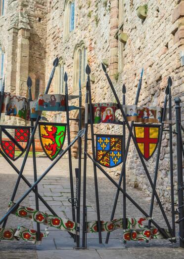 Wrought iron gates with stained glass shields and flags leading into a castle.