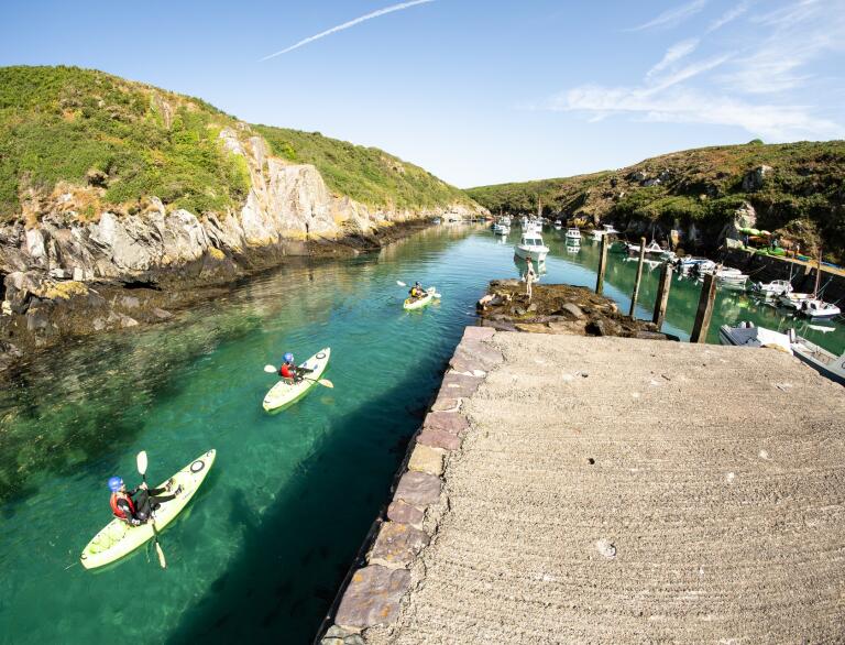 Kayakers passing dramatic cliffs in a harbour.