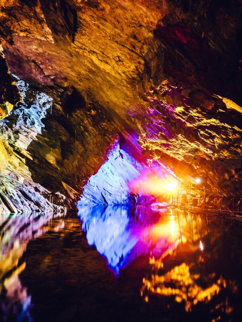 Underground slate cavern colourfully lit and reflecting in the water.