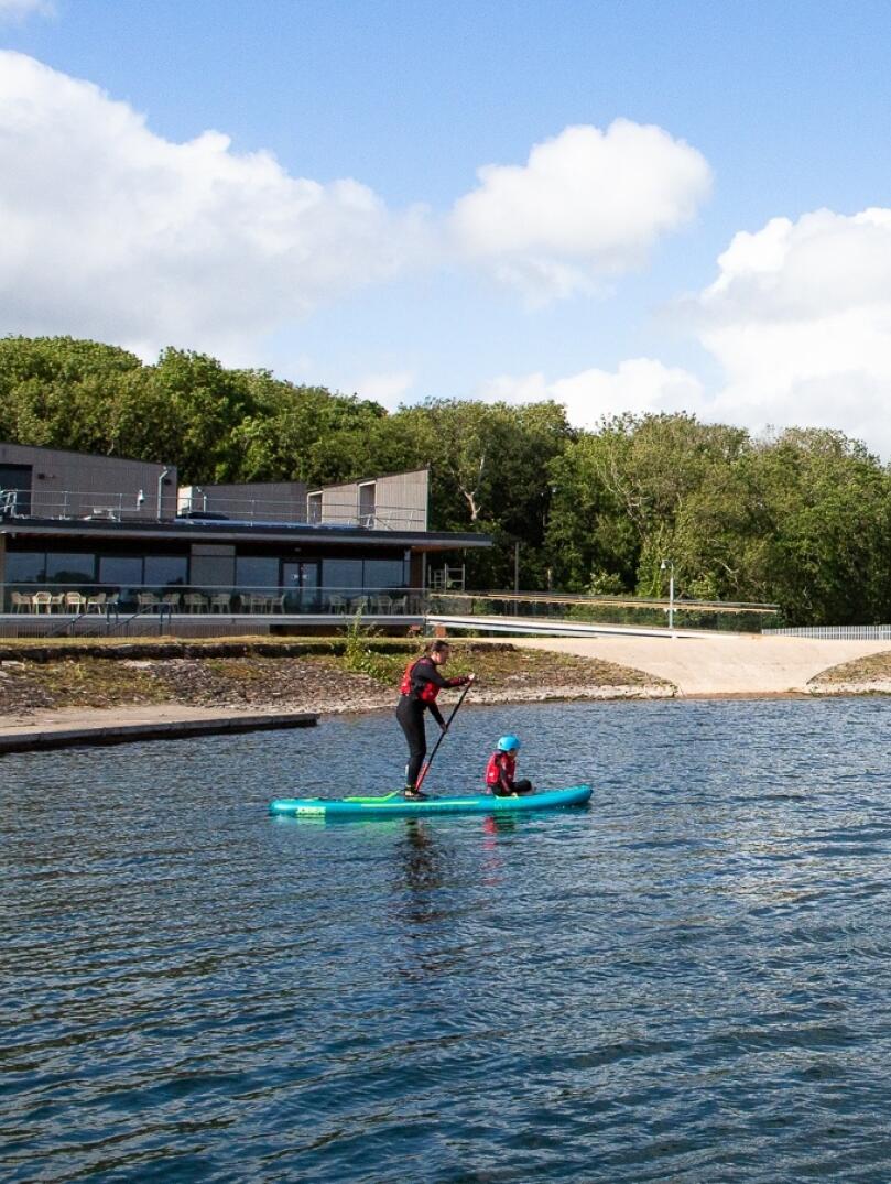 Stand up paddleboarders on the water next to a visitor centre.