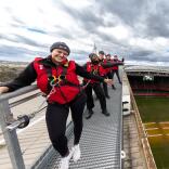 Group of people in safety gear on a roof at a sports stadium.