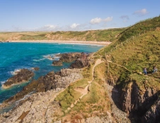 Walkers on a rugged coastal path with views toward a golden beach.