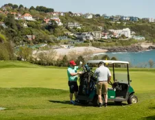 Two guys selecting clubs from their golf buggy with views of the bay beyond.