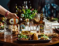 A person pouring lager into a glass on a table with plates of food.