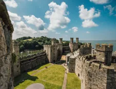 Looking down at a castle courtyard from a tower with sea views beyond.