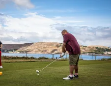 A man about to take a swing at a golf ball, with views of the bay beyond.