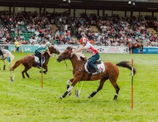 Riders on horseback in a showground entertaining a crowd.