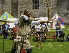 A man dressed in a medieval outfit performing archery in castle grounds.