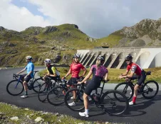 Group of cyclists taking a break by a dam and mountains.
