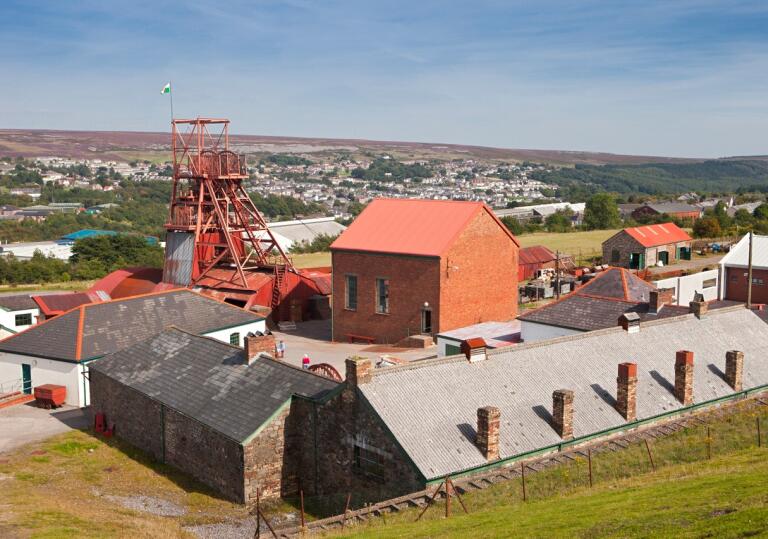 Colliery buildings and a pit head overlooking a town in the South Wales valleys.