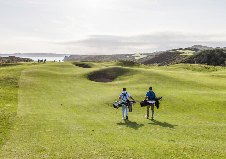 Golfers walking to the next tee with views of the coastline.
