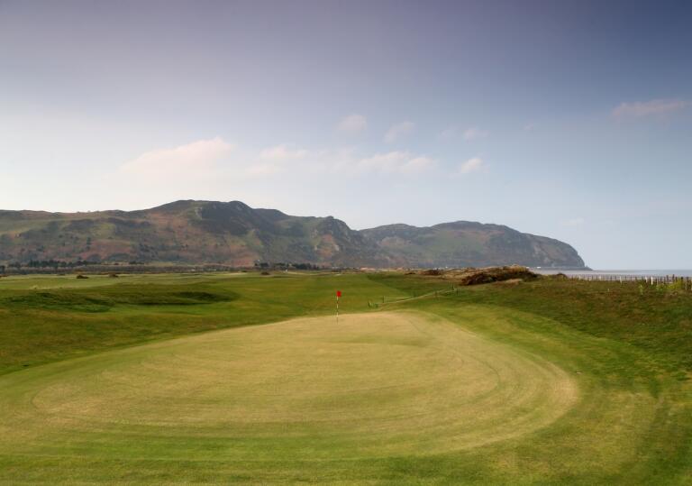 The green on a golf course with views of the coastline and cliffs beyond.