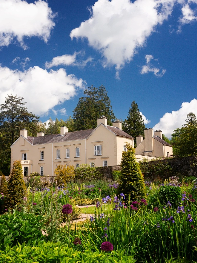 A grand house set in colourful gardens on a sunny day.