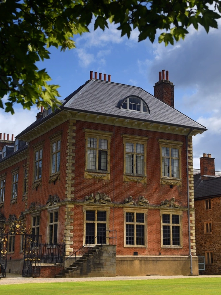 A side view of a grand house with orange brickworkand black and gold railings.