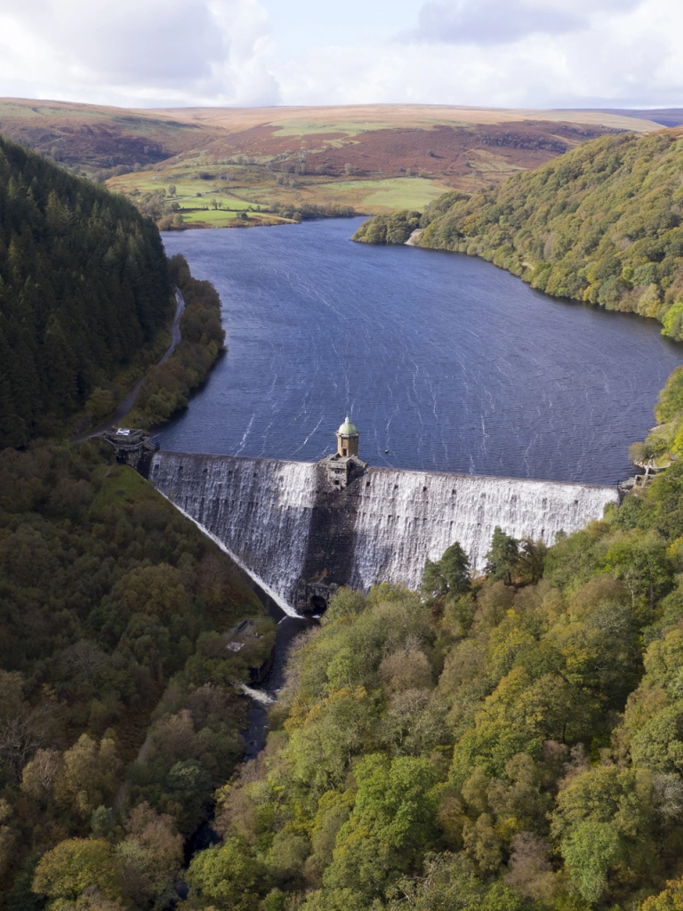 An aerial shot of the river held back by the dam surrounded by forest.