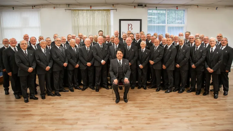 A large group of male singers in suits smiling at the camera.