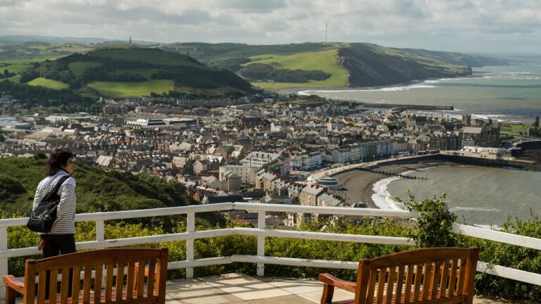 Looking down toward a coastal town and coastal path from a seating area on a hill.