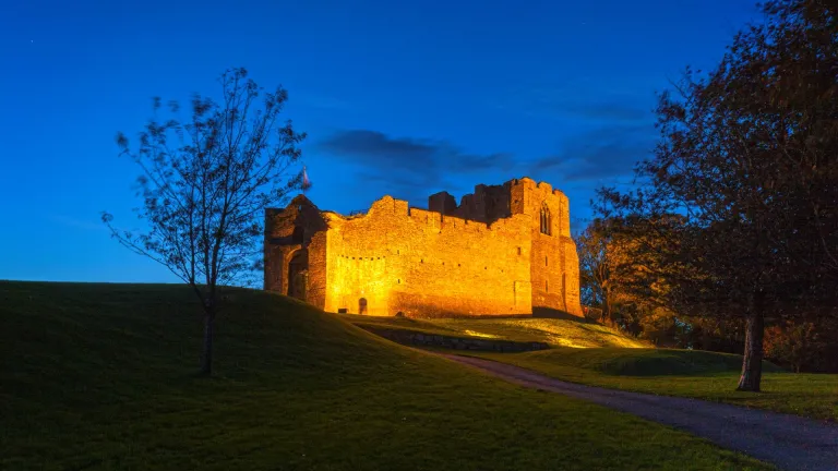 Oystermouth Castle lit up with an orange glow surrounded by tree silhouettes at twilight.