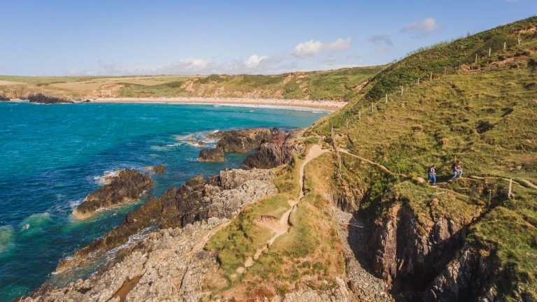 Walkers on a rugged coastal path with views toward a golden beach.