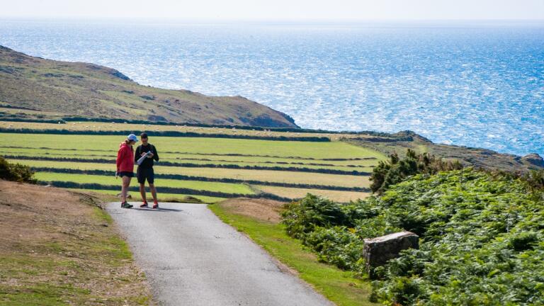 Two walkers looking at a map on a coast path with views of the sea and landscape beyond.