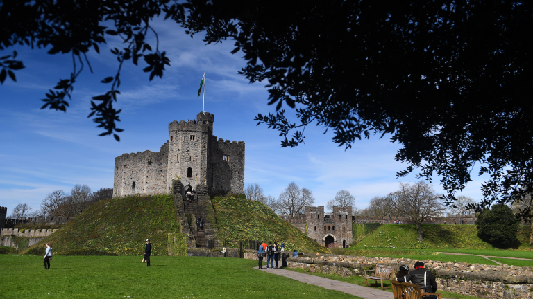 People walking up to The Keep, a tower at Cardiff Castle framed by a tree in the foreground.
