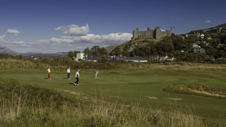 Four people playing golf at Royal St. David's Golf Club with Harlech castle above.