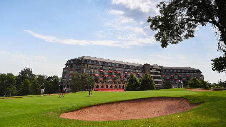 Golfers near the bunker with the Celtic Manor Resort Golf Club hotel in the background.