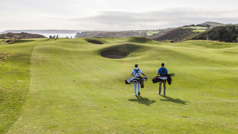 Golfers walking to the next tee with views of the coastline.