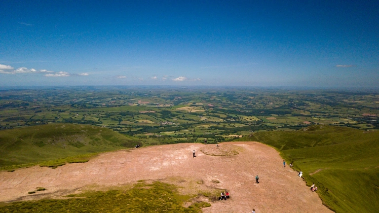 Aerial view of the green plains below from the top of Pen y Fan with blue skies.