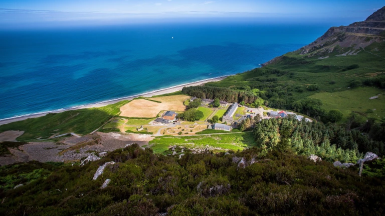 Aerial shot of Nant Gwrtheyrn surrounded by green landscape and the sea.