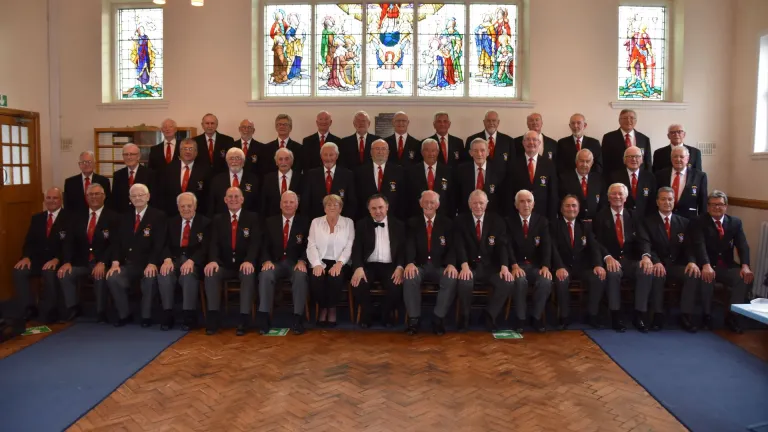 A choir posing for the camera with stained glass windows in the background.
