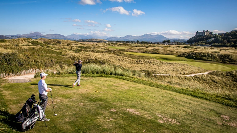 Golfers on a golf course with a castle and mountains in the background.