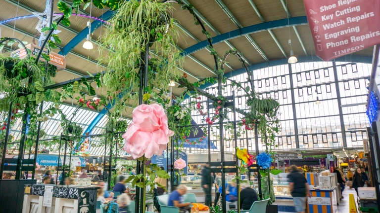 Eating area covered in foliage and flowers, and stalls in a large indoor market.