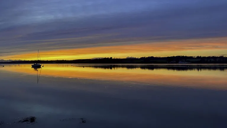 Dramatic colourful sunset over the coast with a boat on the water.