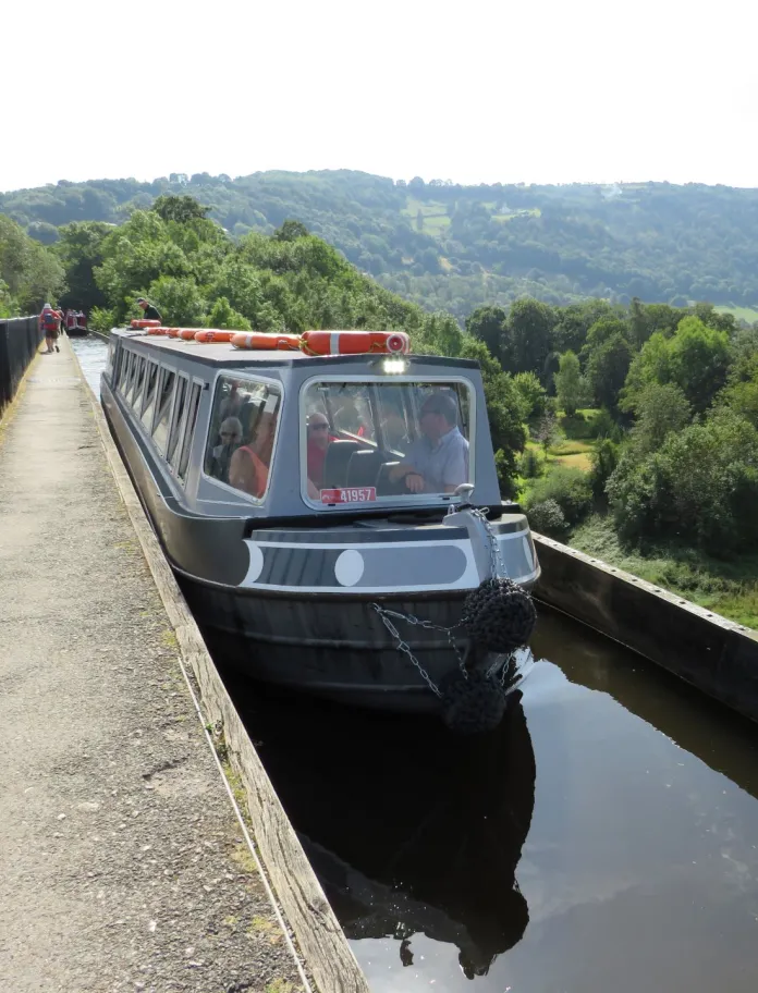 A narrowboat travelling along an aqueduct on a sunny day.