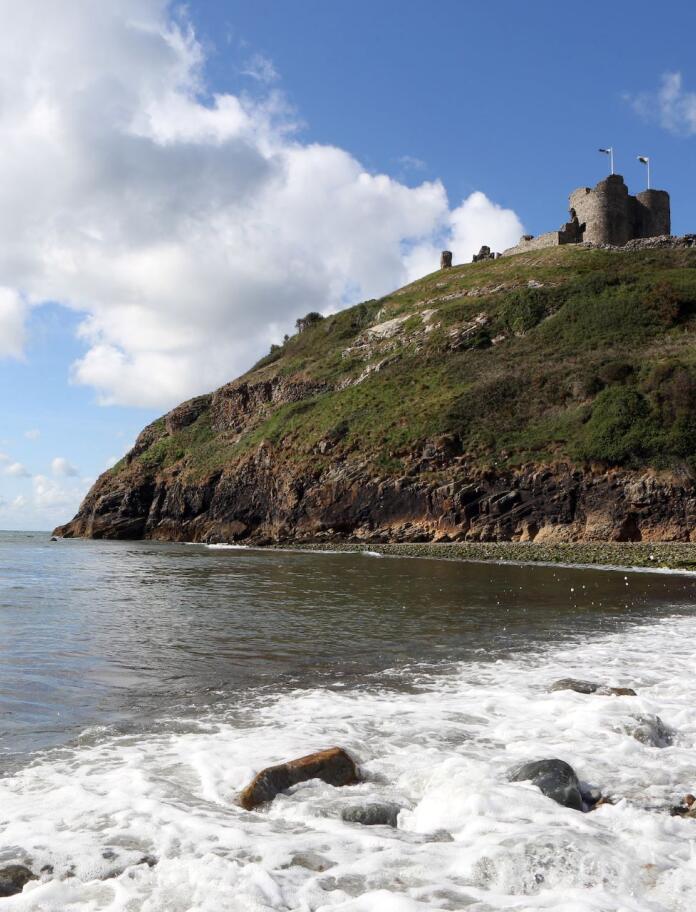 Standing on the shoreline with waves hitting the beach, looking up to Criccieth Castle on a hill.