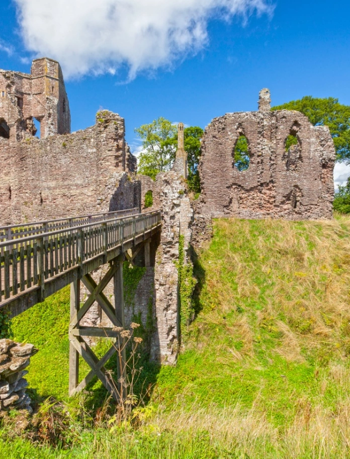 A drawbridge leading to the ruins of a castle on a mound.