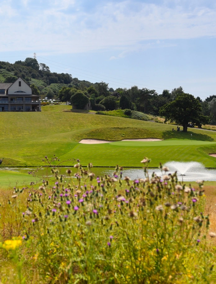 Golf course featuring bunkers and a water feature with the clubhouse beyond.