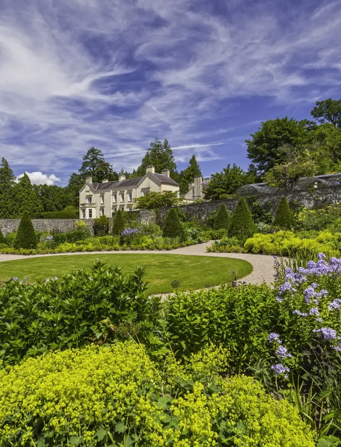 A view of Aberglasney House surrounded by the garden with dramatic blue sky and wispy clouds.