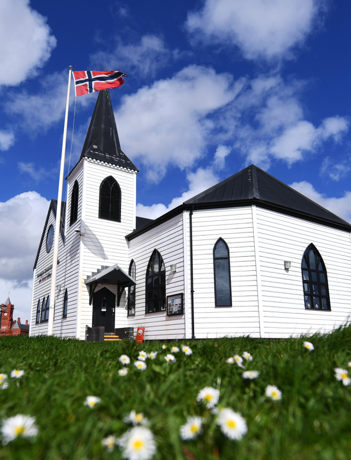 View of the Norwegian Church behind a lawn full of daisies.