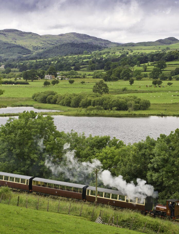 Bala Lake Railway steam train travelling along the lakeside with mountains in the background.