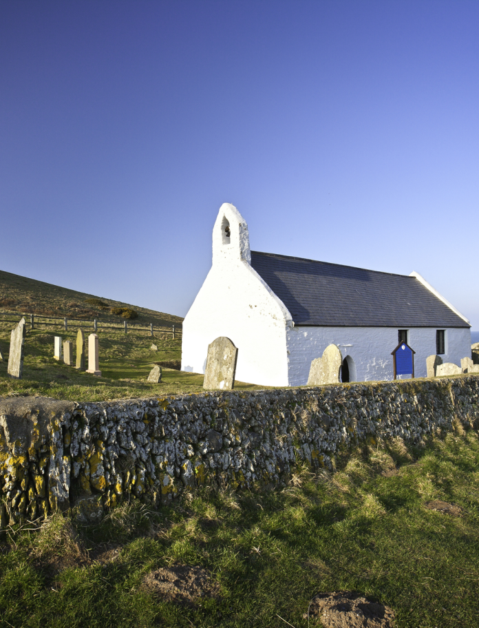 A small white church and graveyard isolated amongst the coastline and fields.