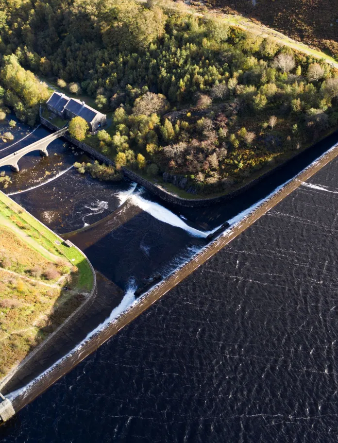 Arial shot looking onto the green trees, reservoir and dam.
