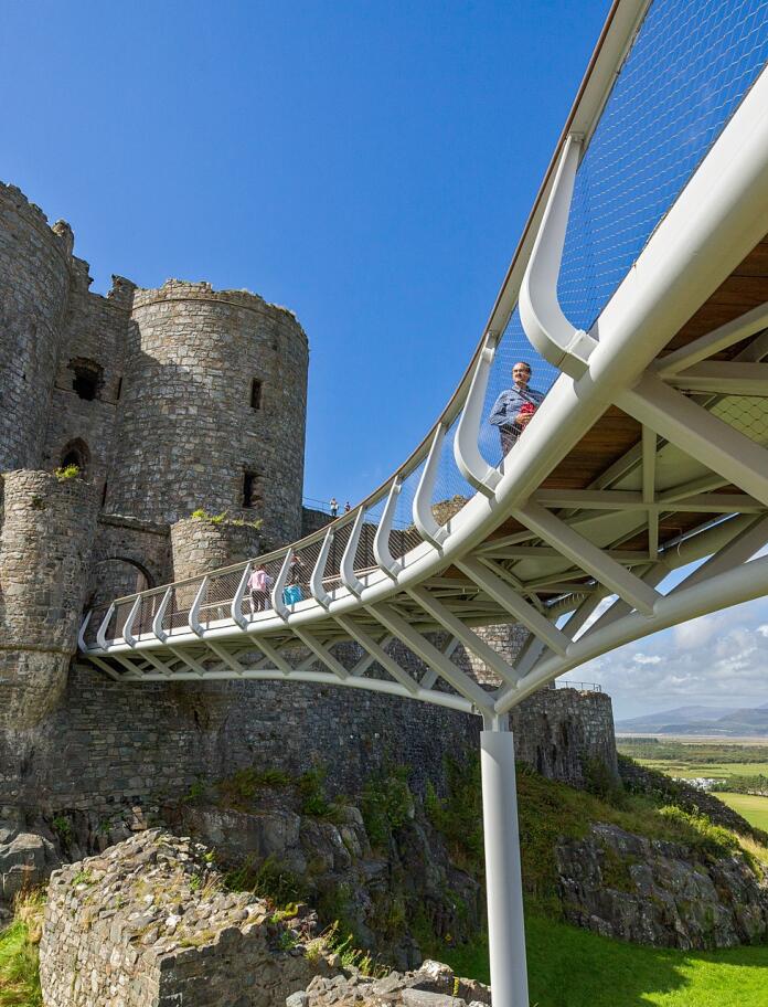 People walking over a sky bridge leading to a castle.
