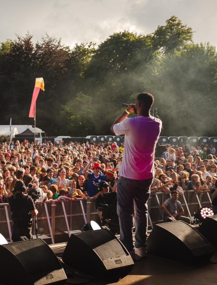 A guy on stage at a festival facing the crowd beyond.